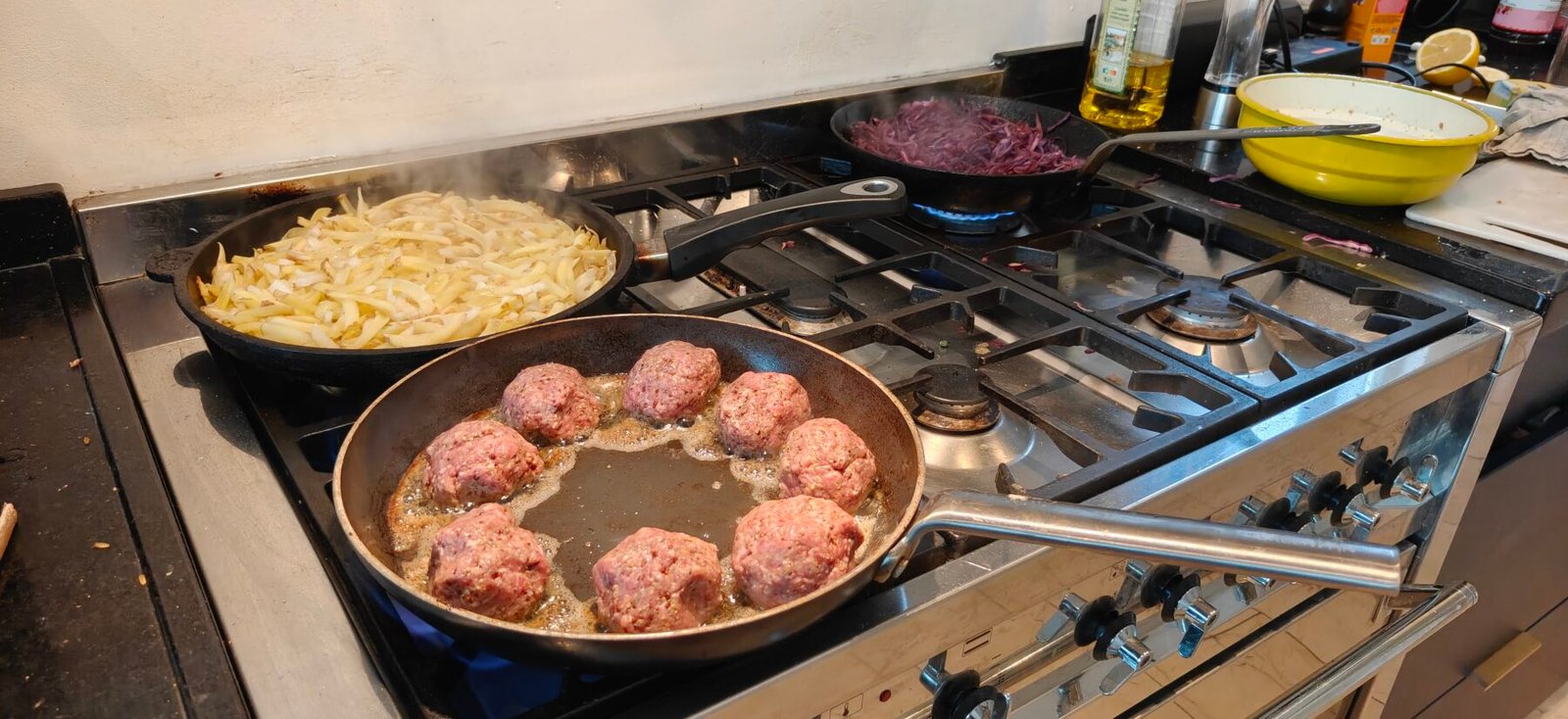 Drie pannen op het fornuis: acht gehaktballen, een grote rösti van aardappelreepjes en rode kool