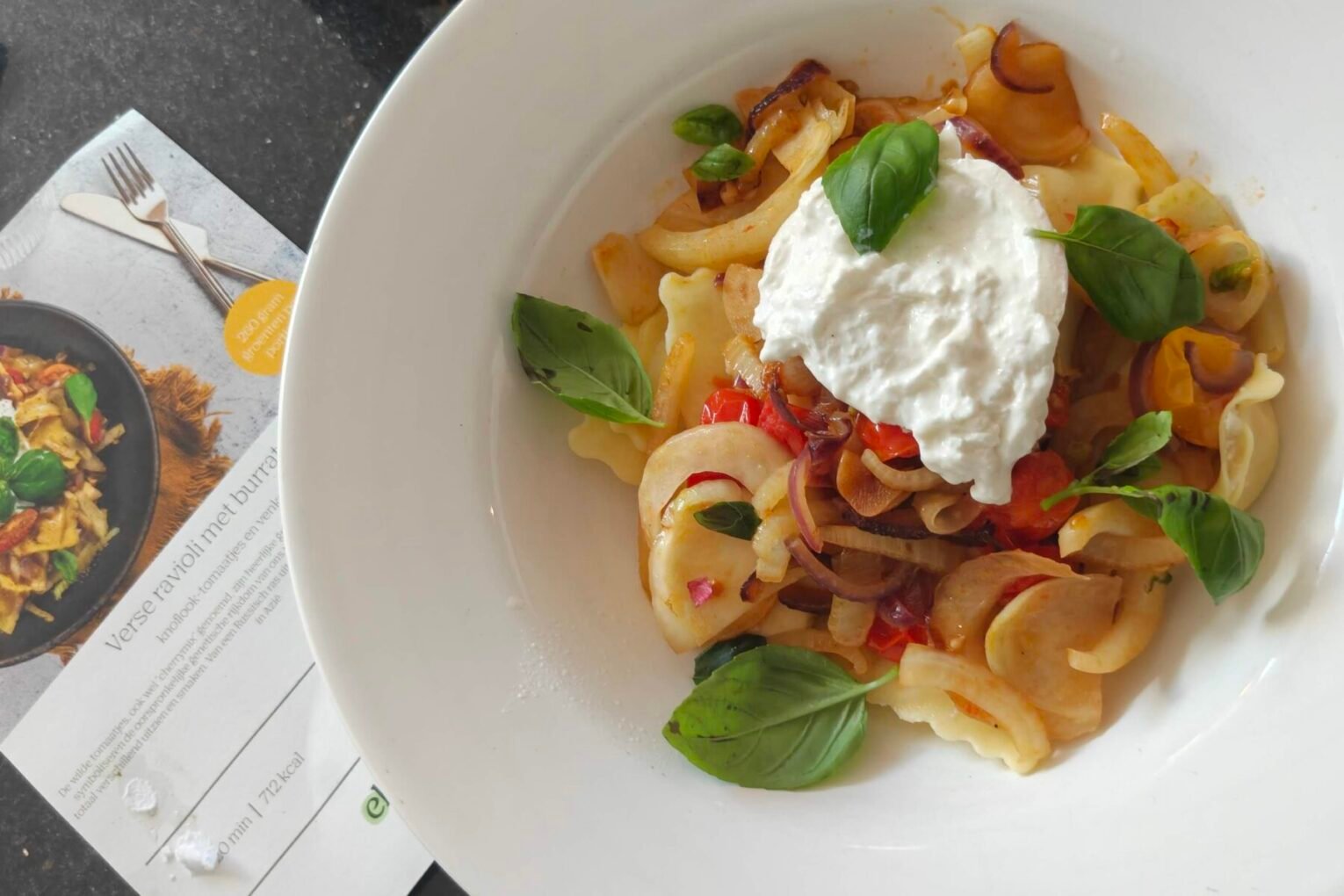 Bord met verse ravioli, burrata, gebakken venkel, tomaatjes en basilicum van Ekomenu, met de receptkaart ernaast